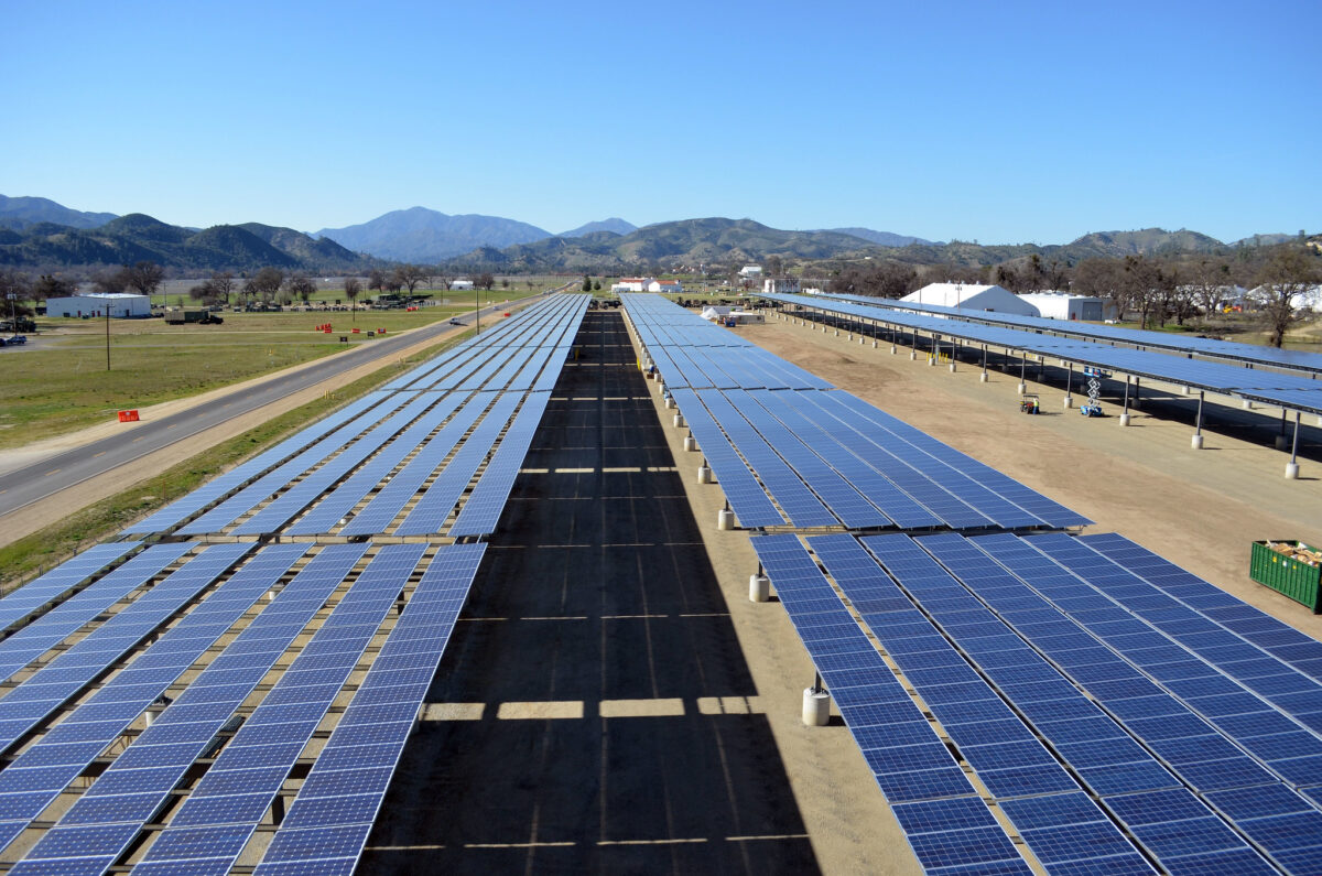 Solar panels extend toward distant mountains, blue sky.